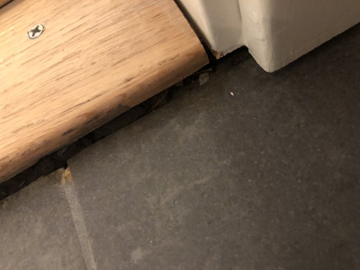 Badrumströskel med öppna mellanrum mellan tröskel och golv, synlig skruv och klinker.