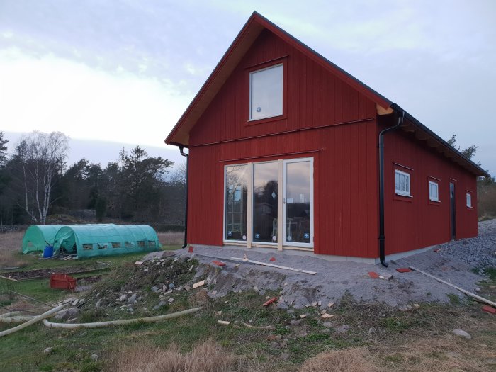 Nybyggt rödmålat garage och kontor i ladustil med takutsprång och stora fönster, under konstruktion.