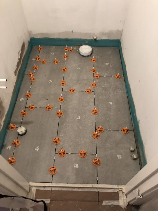 Klinkergolv under installation med orange utjämningsskruvar mellan plattorna i ett rum.