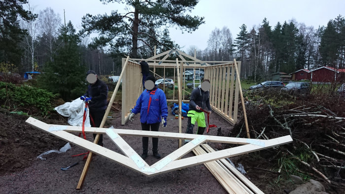 Personer förbereder att resa en takstol på en byggarbetsplats med spännband och verktyg.