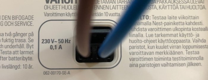 Närbild av en Nest brandvarnares elmatningskontakt med tekniska specifikationer 230V – 50 Hz, 0.1 A synliga.