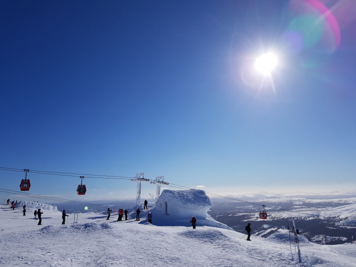 Solig dag i Åre med skidåkare, skidlift och snötäckta berg.