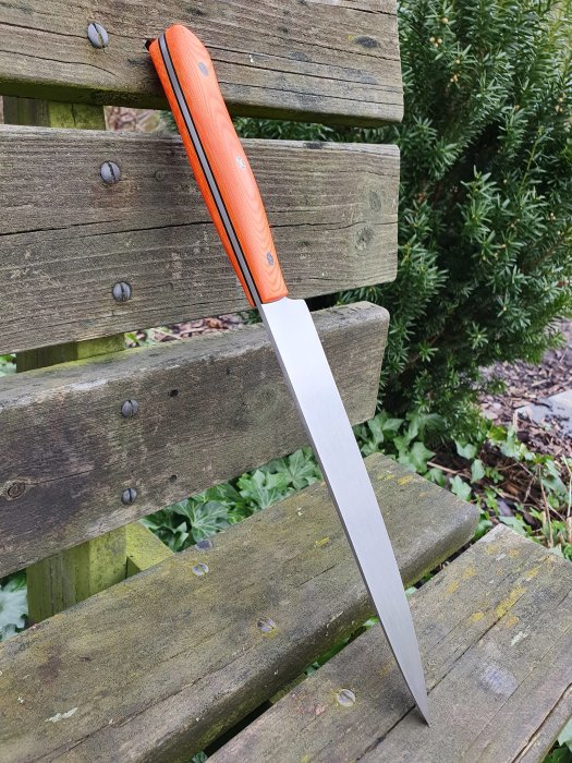 Kniv med orange micartahandtag och svart G10-mellanlägg på träbänk.