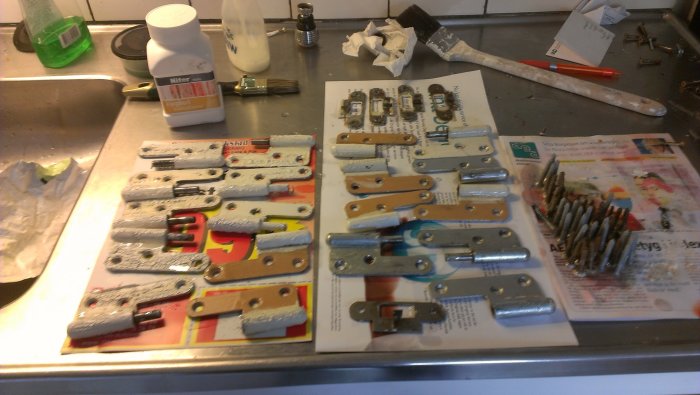 Renoverade gångjärn utan färg, placerade på tidningspapper bredvid färgborttagningsmedel.