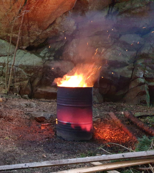 Eldtunna brinner med flammande eld framför en klippvägg, avfall från renovering bränns.