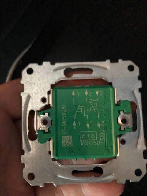 Hand håller en väggströmbrytare med synlig kabelanslutning och kopplingsschema.