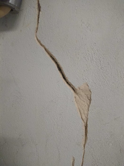 Vägg med spricka och löst puts som kräver reparation.