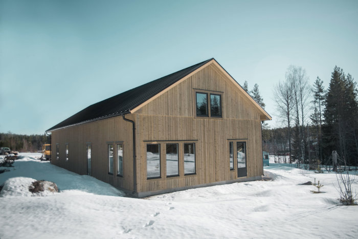 Modern träklädd villa med snedtak i snölandskap under klar himmel.