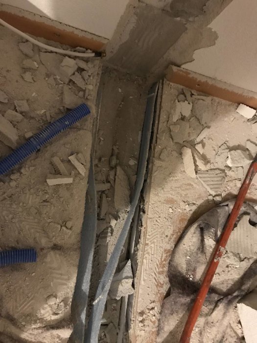 Avlägsnad vägg som lämnat efter sig en gapande springa mellan två betongytor med synliga rör och kablar.