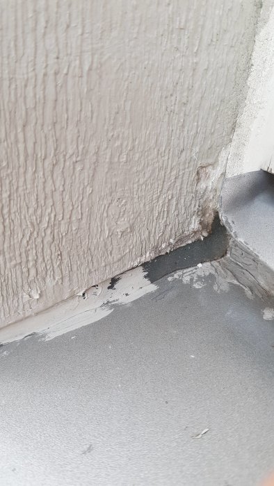 Skadad vägg och golv i hörnet vid fönster med tecken på möjlig vattenläckage.