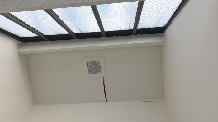 Innertak med synlig del av genomskinliga glasskivor på taket, ljusinsläpp, takbalkar och ventilation.
