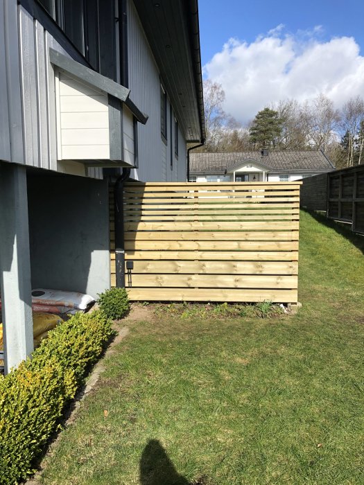 Nybyggt trästaket vid husvägg med matningskabel framdragen och gömd, på en solig dag.