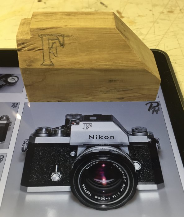 Ekbit utskuren till formen av en Nikon F-kamera spegelsökare ovanpå ett foto av Nikon F-kameran.