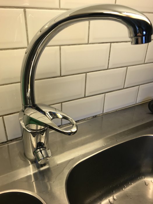 Kromad morablandare som läcker, monterad vid köksvask med vita kakelplattor i bakgrunden.