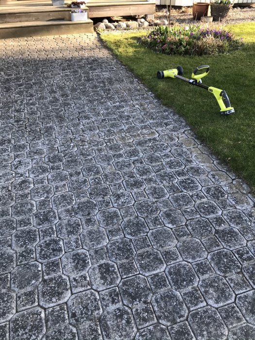 Nybelagd gångväg av sten framför en trappa med en Ryobi grästrimmer på gräsmattan.