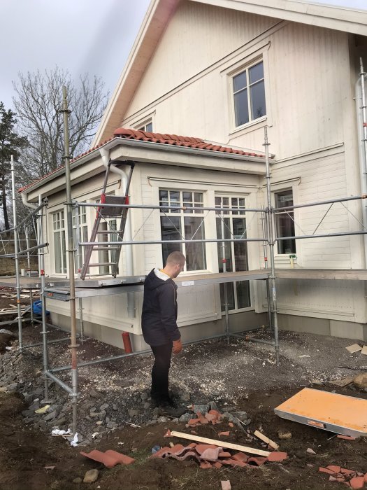 Hus under renovering med fasad färdigställd, ställningar runt huset och person som betraktar arbetet.