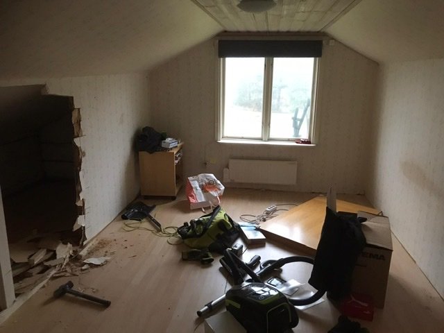 Renoveringsarbete i sovrum med öppet tak, verktyg på golvet och ett fönster som ger ljus.
