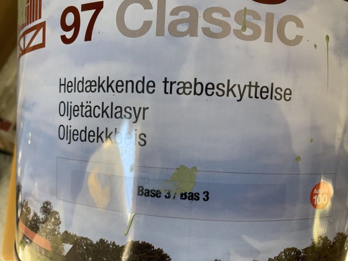 Delvis skymd etikett på en burk Flügger 97 Classic oljetäcklasyr med reflektioner och färgstänk.