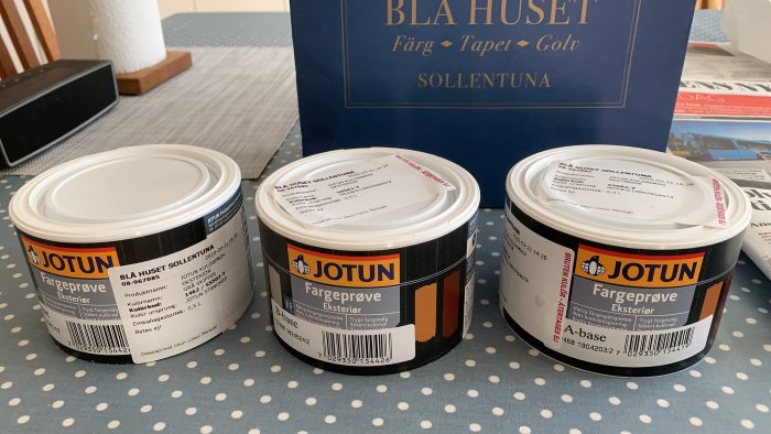 Tre burkar med Jotun färgprover på ett bord, med en Blå Hus Sollentuna affärspåse i bakgrunden.