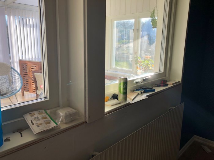 Ett orenoverat sovrum med två fönster utan foder, verktyg och renoveringsmaterial på fönsterbrädan.