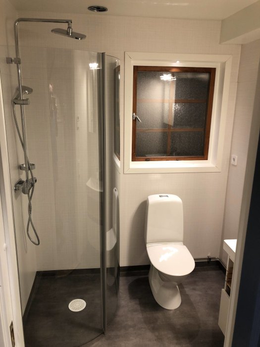 Renoverad WC med duschkabin, toalett och våtrumsmatta Raw Concrete Dark Grey samt tapet i ljusgrått.