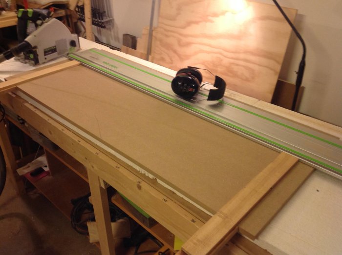 Verktyg och spillvirke på arbetsbänk medan en mdf-skiva förbereds för sågning.