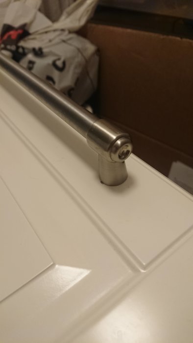 Metallhandtag på vit kökslucka, troligen från Ikea, med skruv på framsidan.