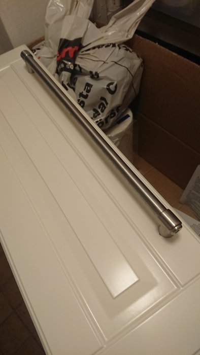 Stående bild av ett långt silverfärgat metallhandtag monterat på en vit lucka, möjlig Ikea-produkt.