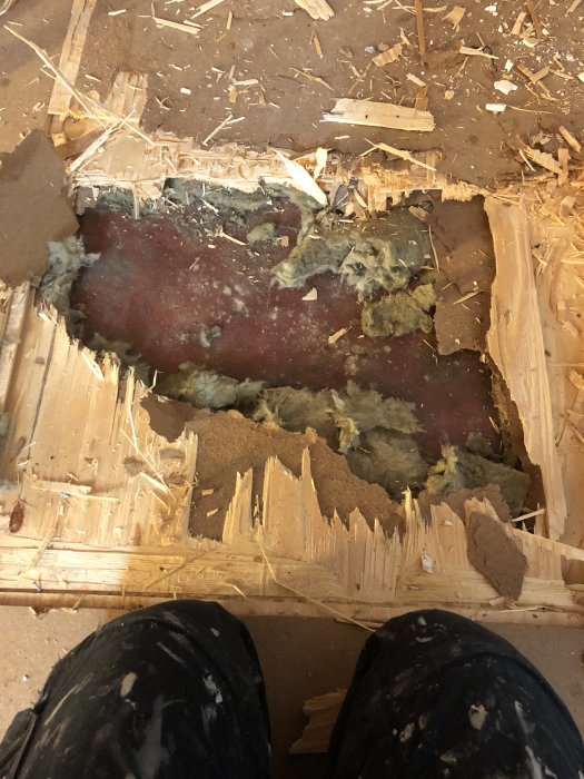 Utsikt över ett golv under rivning, med trasiga träbitar och dålig betong synlig i ett hål.
