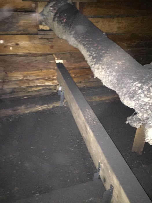 Inredningsbild av vind med synligt bjälklag och timmerväggar, isolering synlig.