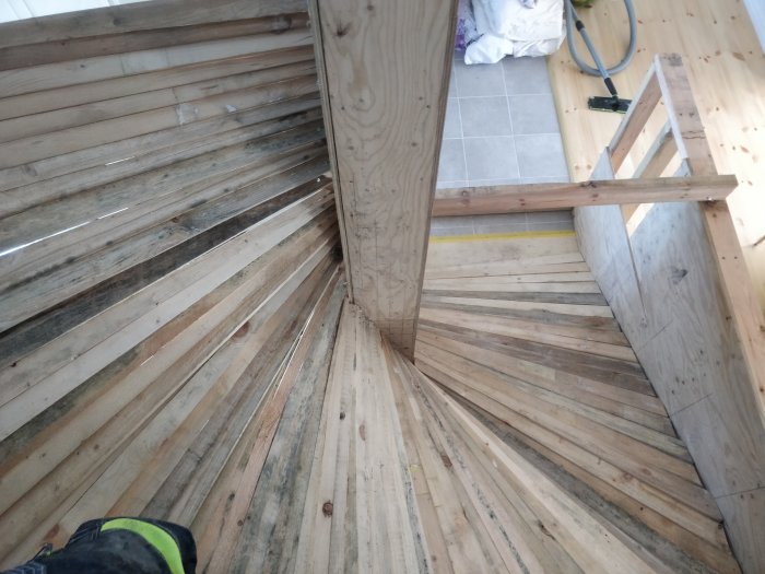 Ovanifrån bild på en nyligen gjuten spiraltrappa i trä under konstruktion, plywood synligt, utan räcken.