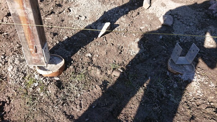 Två betongplintar i marken med metallbeslag för stolpar, en meter från varandra.