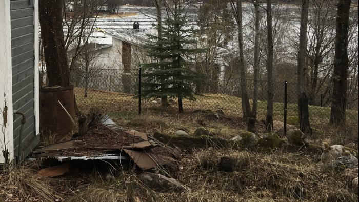 Bild på delvis nedmonterat staket gjutet i en berggrund, med natur och en gran i bakgrunden.