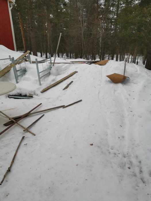 Snötäckt utomhusyta med uppsamlat byggavfall bestående av träplank och metallen som ligger på marken.