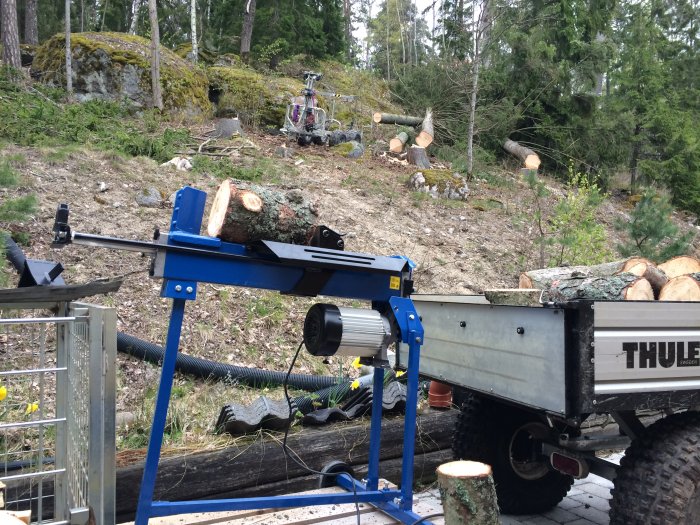 Vedklyv av märket Vimmerby med stock på plattformen utomhus nära en upphuggningsplats.