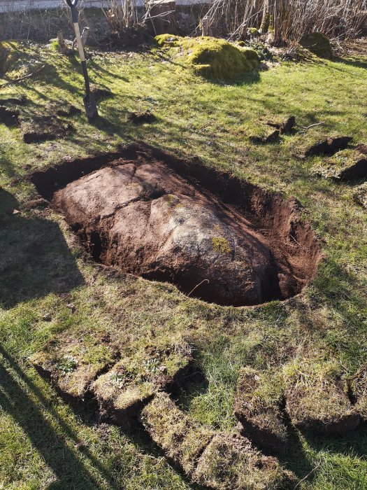 Stor bergknalle i ett grävt hål i en trädgård som förberedelse för installation av automover.