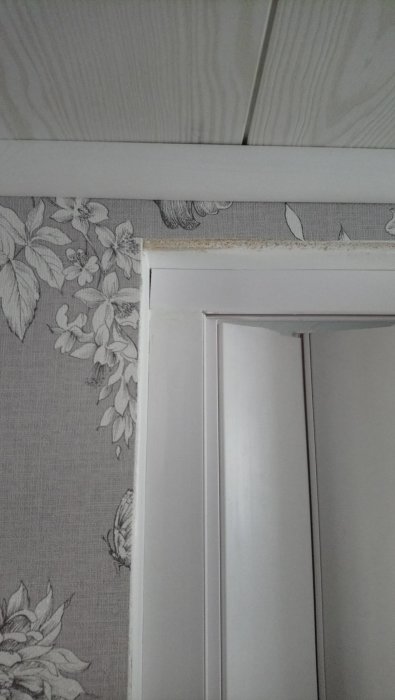 Detaljbild av anslutning mellan vit dörrkarm och blommigt tapetserad vägg med en synlig skarv.