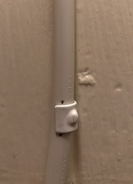 Utanpåliggande vit elkabel fäst i vägg med klammer som har svarta märken vid varje fästpunkt.