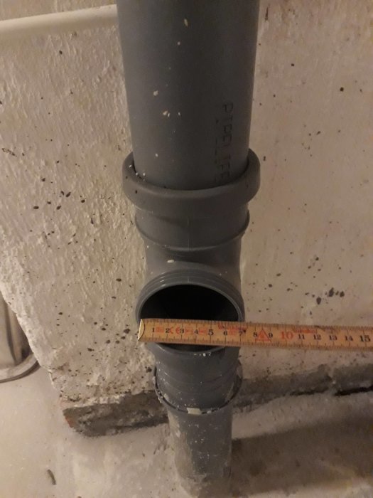 Grå PVC-avloppsrör med ett öppet inspektionslock och ett måttband som visar dimensionerna.