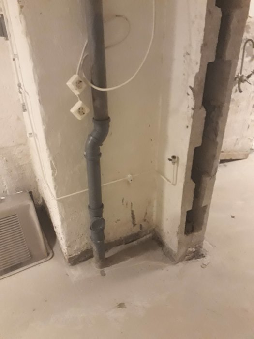 Avloppsrör i betongvägg med inspektionslock och eluttag som förberedelse för inkoppling av tvättmaskin.