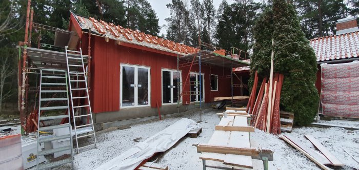 Rödfärgat hus under renovering med tegel och nyinstallerade fönster och dörrar, snö på marken.