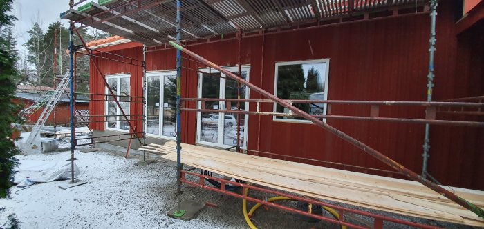 Exteriör av hus under renovering med ställningar, nymonterade fönster och träplankor, snötäckt mark.