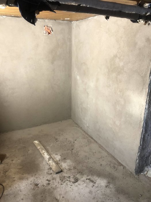 Nyligen putsade väggar i ett hörn av ett rum med en murarslev på betonggolvet.