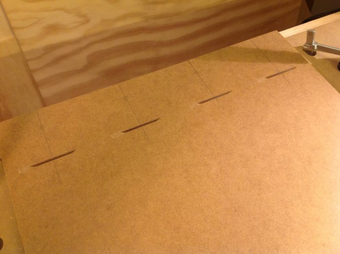 Frästa kexskåror i MDF-panel med linjer för precision, intill träbit och tving.