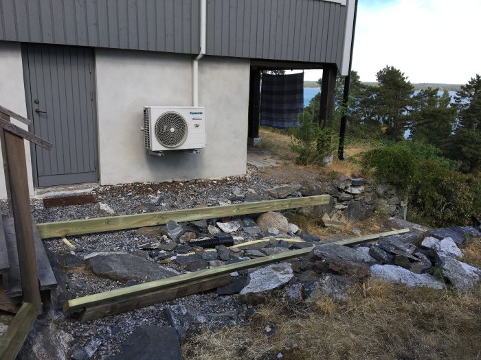 Nybyggd trätrappa under konstruktion utanför ett gråmålat garage med havsutsikt i bakgrunden.