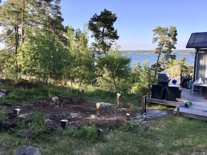 Tom plats med stubbar där gammal friggebod rivits, utsikt över vatten, nära nybyggt däck.