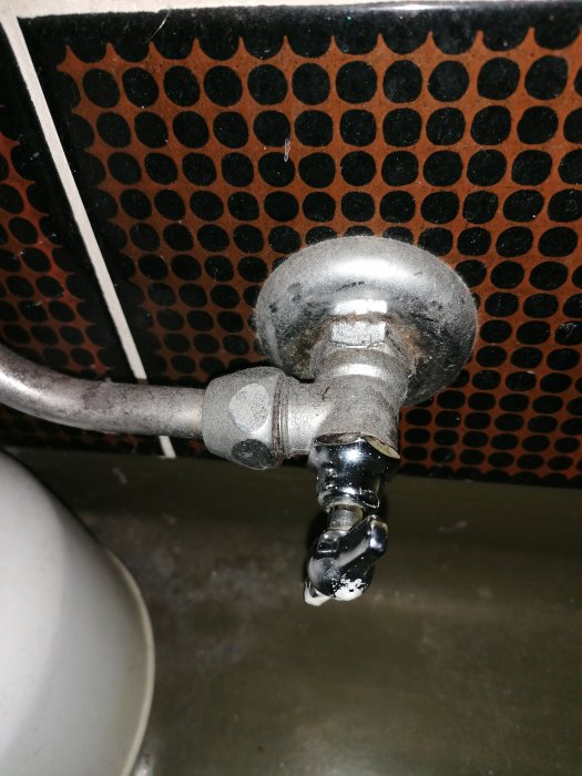En gammal fastrostad avstängningskran för vatten till wc-stol, monterad på 16mm kopparrör, med slitage och kalkavlagringar.