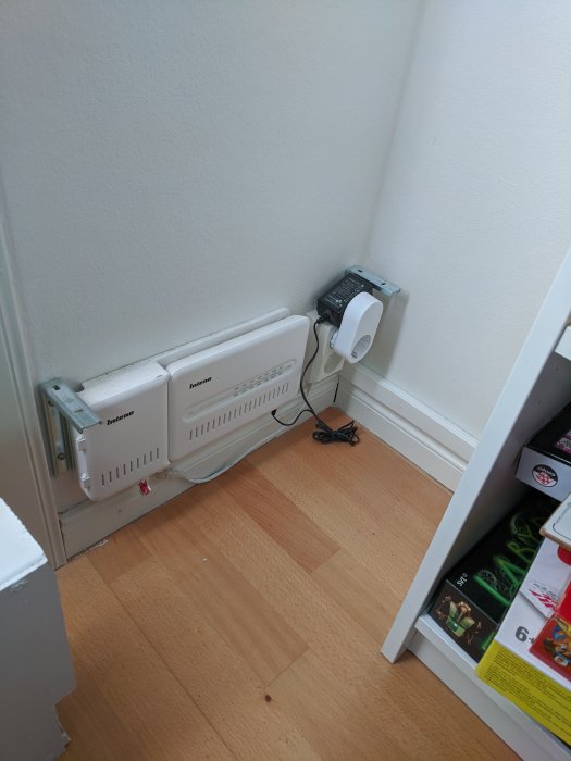 Installation av en vit elektrisk radiator och programmerbar termostat i ett hörn vid ett trägolv.