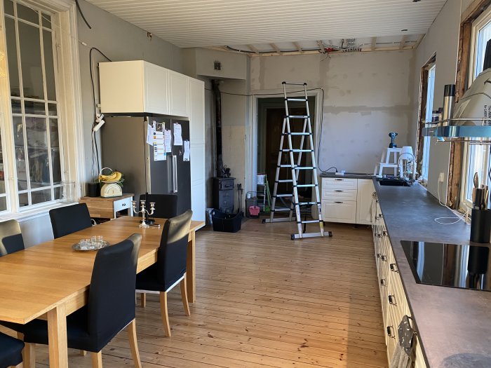 Kök under renovering med otillslutna väggar, trägolv, matbord och delvis monterade vitvaror och skåp.