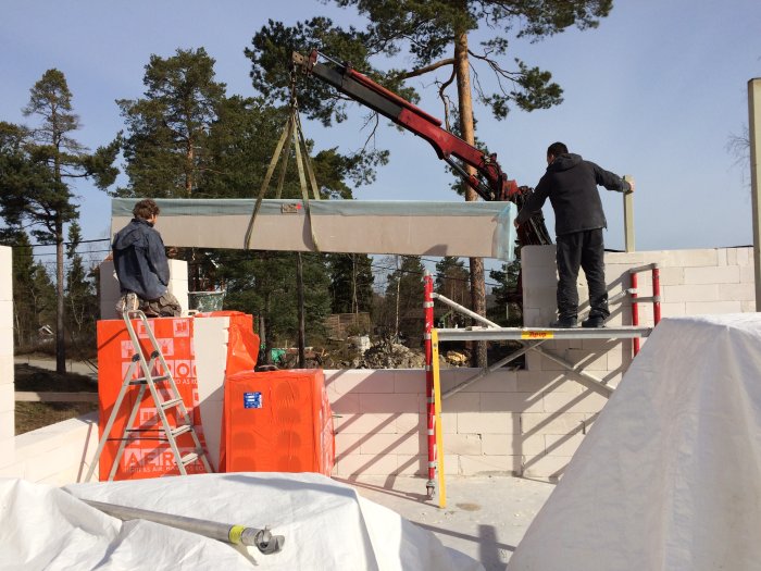 Arbetare använder kran för att lyfta en betongbalk på plats vid en byggarbetsplats.